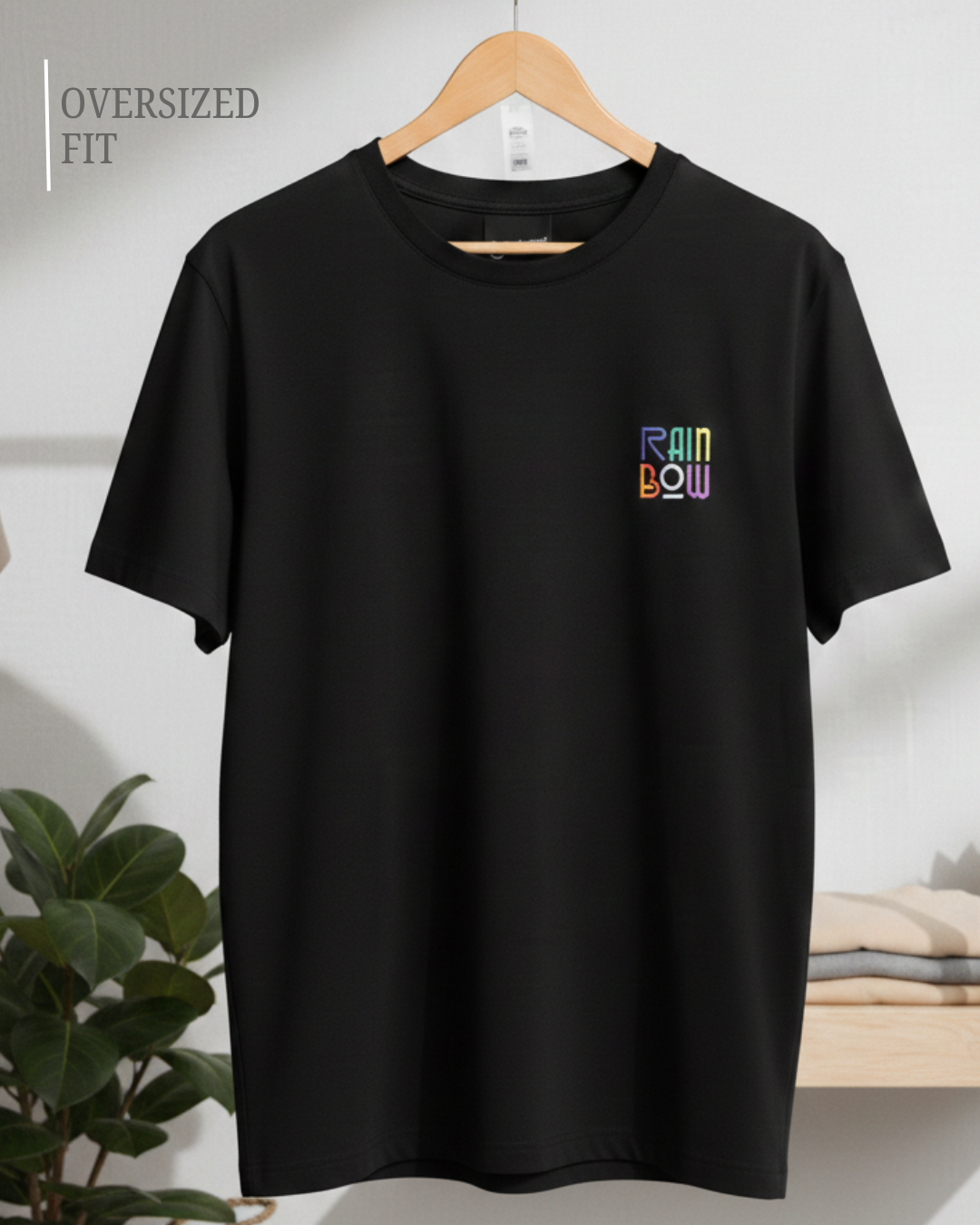 Black oversized fit t-shirt with small rainbow logo hanging on wooden hanger in minimalist studio background