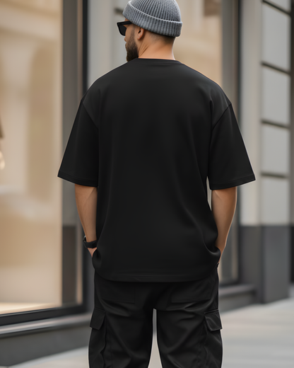 Man wearing a black t-shirt and cargo pants standing in front of a store window.