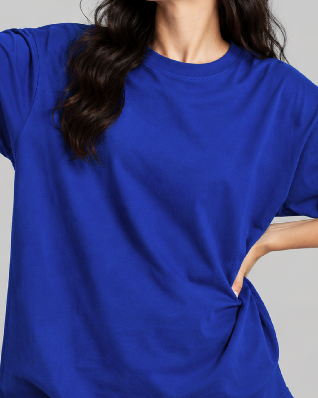 A close-up of a person wearing a bright royal blue short-sleeve crewneck t-shirt, showing the fabric drape and side pocket detail against a neutral gray background from white bear brand