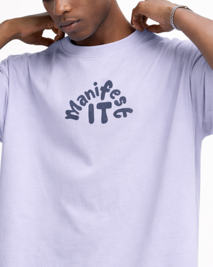 Person wearing a light purple t-shirt with 'Manifest IT' text design.