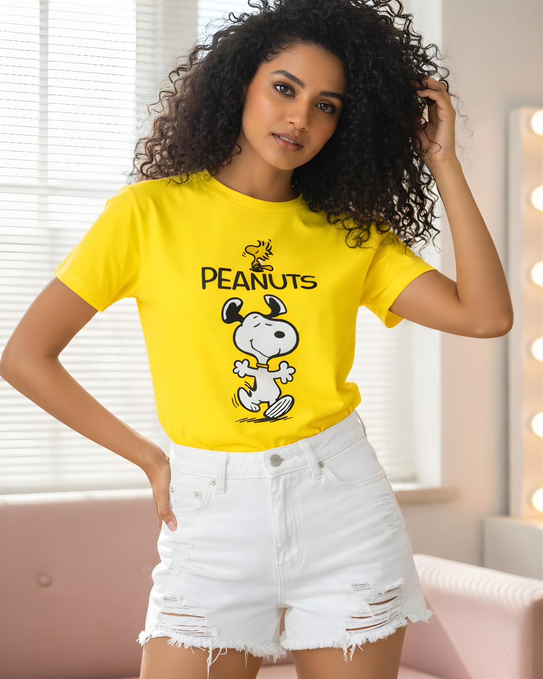 Woman wearing a peach #FFDEC6 Peanuts Snoopy graphic T-shirt paired with white distressed denim shorts in a bright indoor setting.