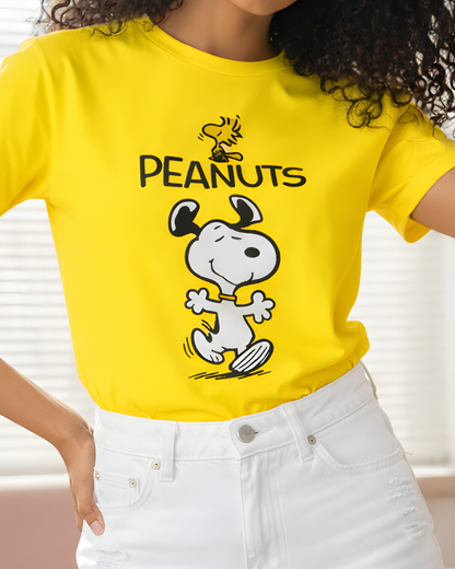 Woman wearing a yellow Peanuts Snoopy graphic T-shirt paired with white distressed denim shorts in a bright indoor setting.